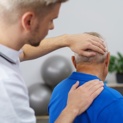 Chiropractor adjusting the neck and shoulder of an older male patient to relieve chronic pain and improve mobility.