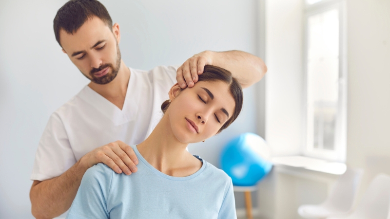 The chiropractor is performing a gentle neck and shoulder adjustment to relieve pain and improve posture in a patient at a chiropractic clinic.