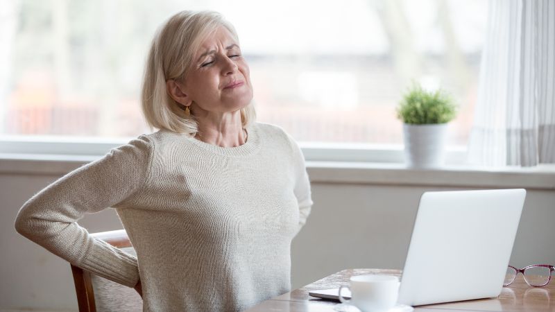 can-a-chiropractor-fix-a-herniated-disc Older woman with back pain from a herniated disc sitting at a desk, searching for chiropractic treatment options.
