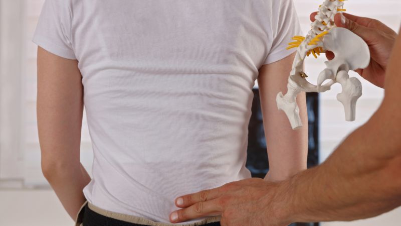 Chiropractor demonstrating spinal alignment and pointing to the lower back area of a patient to explain pinched nerve treatment.